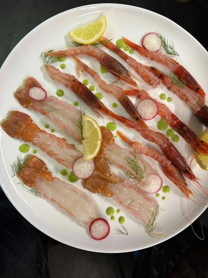 Piatto di sashimi di pesce crudo assortito con spicchi di limone, fette di ravanello e guarnizione verde su un piatto bianco