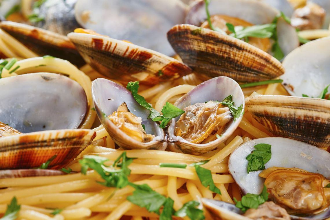 Pasta con vongole, erbe aromatiche e besciamella in un primo piano di un piatto di frutti di mare.