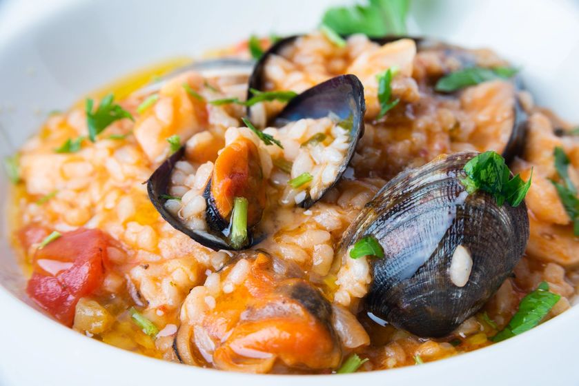 Primo piano di un risotto ai frutti di mare con cozze, gamberi ed erbe aromatiche in una ciotola bianca.