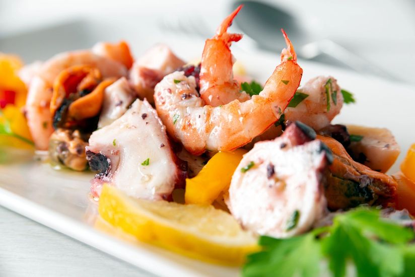 Insalata di gamberi e frutti di mare con spicchi di agrumi, patate e verdure su un piatto bianco.