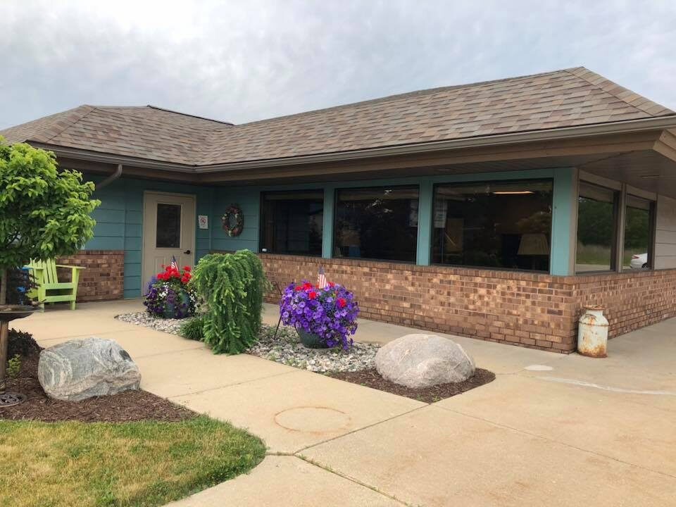 Low-slung building with a brick facade and large windows. Landscaping includes boulders, flowers, and a small lawn.