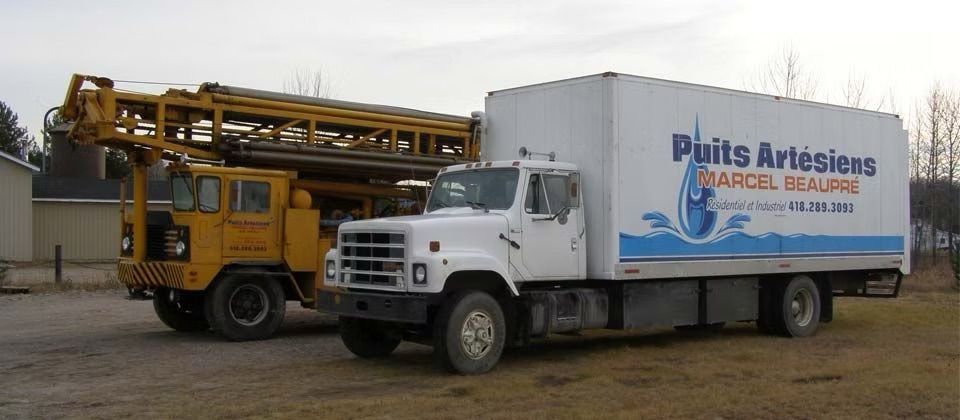 Camion blanc à côté d'une foreuse jaune sur un terrain boueux, portant l'inscription « Puits Artésiens ».