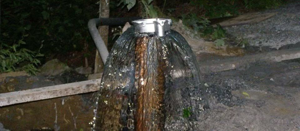 L'eau jaillit d'un tuyau métallique dans un bassin extérieur rocheux la nuit