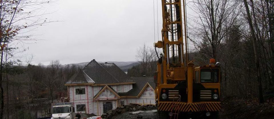 Une foreuse jaune à côté d'une maison en construction dans une zone boisée par temps couvert