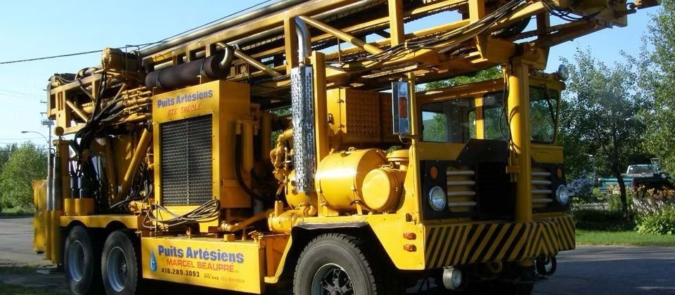 Camion de forage jaune avec longue flèche garé à l'extérieur par une journée ensoleillée
