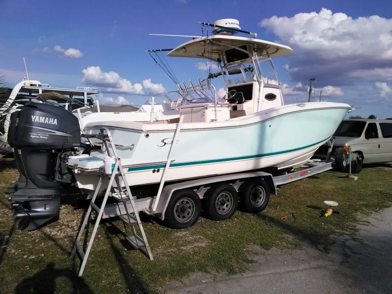 A light blue and white boat on a trailer, with a Yamaha engine, sitting on grass.