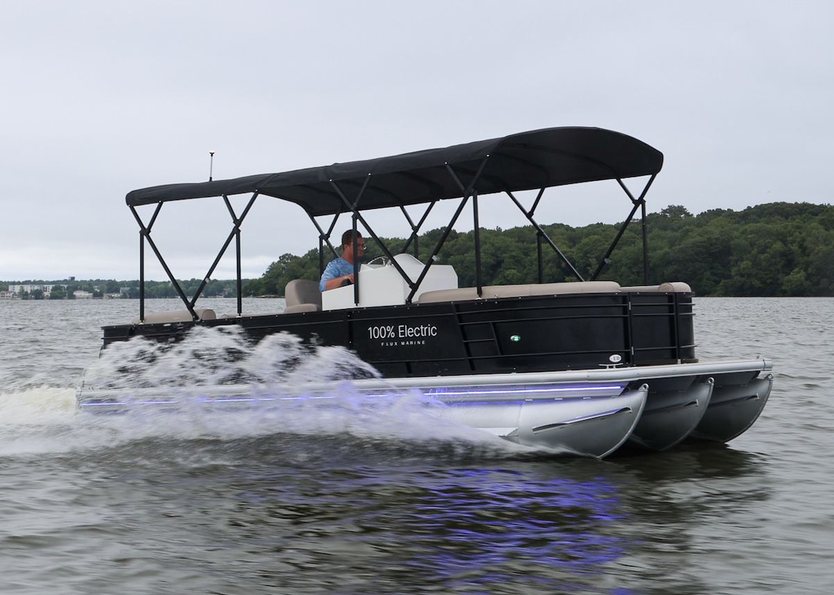 100% electric decal on side of tritoon in water with bimini up over the seating area, and a man in the helm driving the boat
