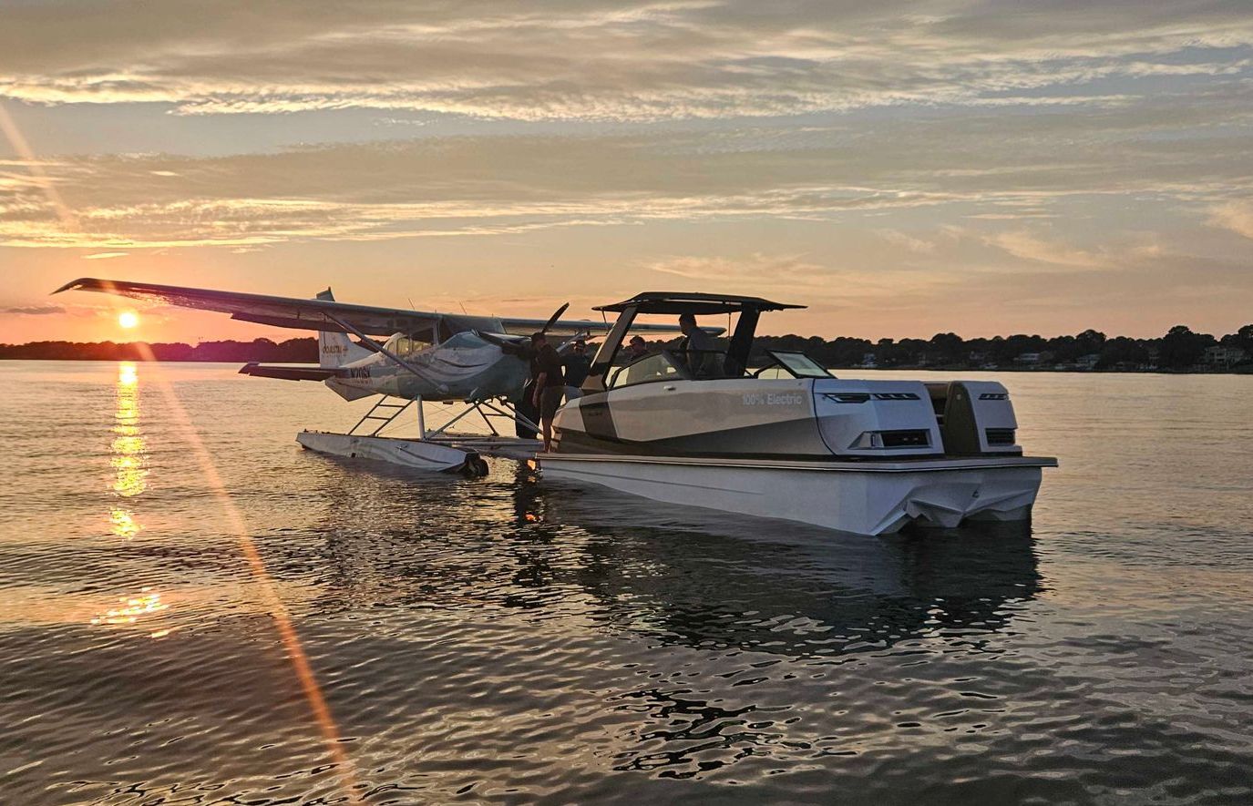A seaplane and a boat are in the water at sunset.