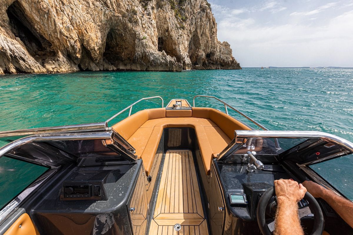 inside of hull on magonis boat with dual side console and full teak flooring open bow area with side seating there is an arm extended in the right corner where a man is driving the boat