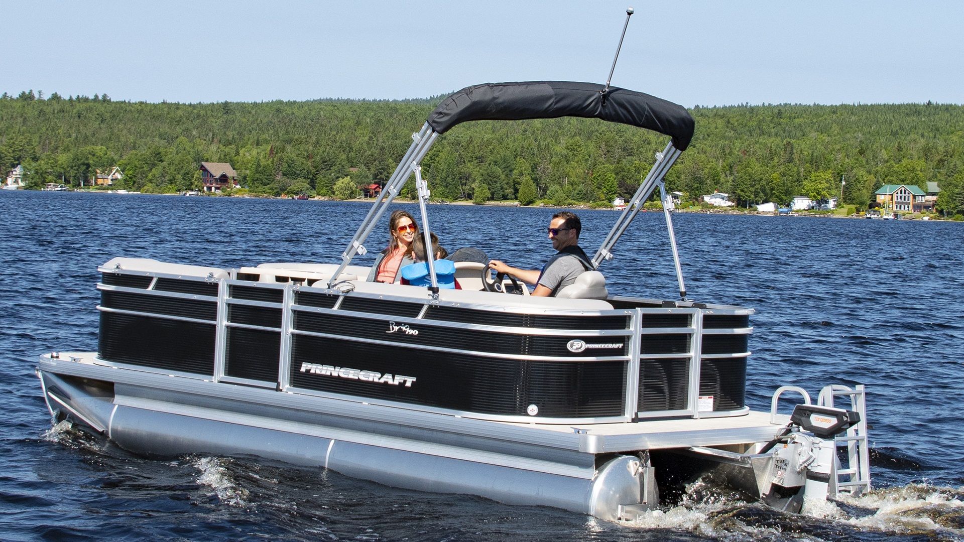 A man and woman are riding a pontoon boat on a lake.