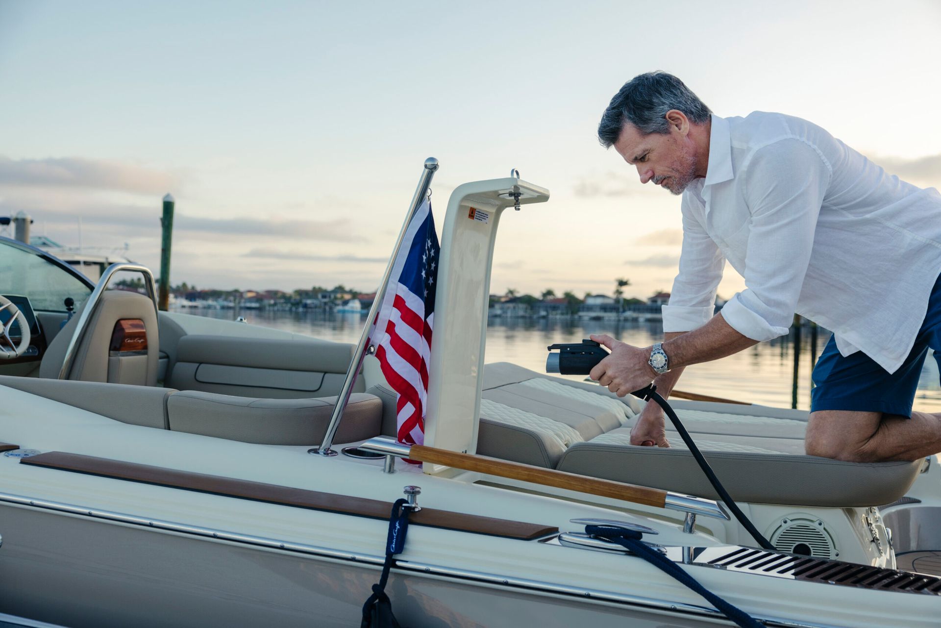 A man is at the dock at sunset, about to plug in his electric boat.
