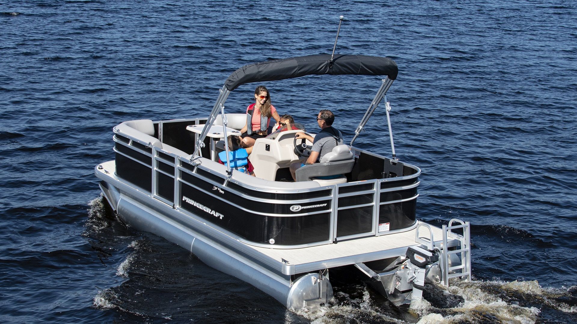 Black Pontoon boat in the open water there is a family on board and an electric motor on the back of the boat.