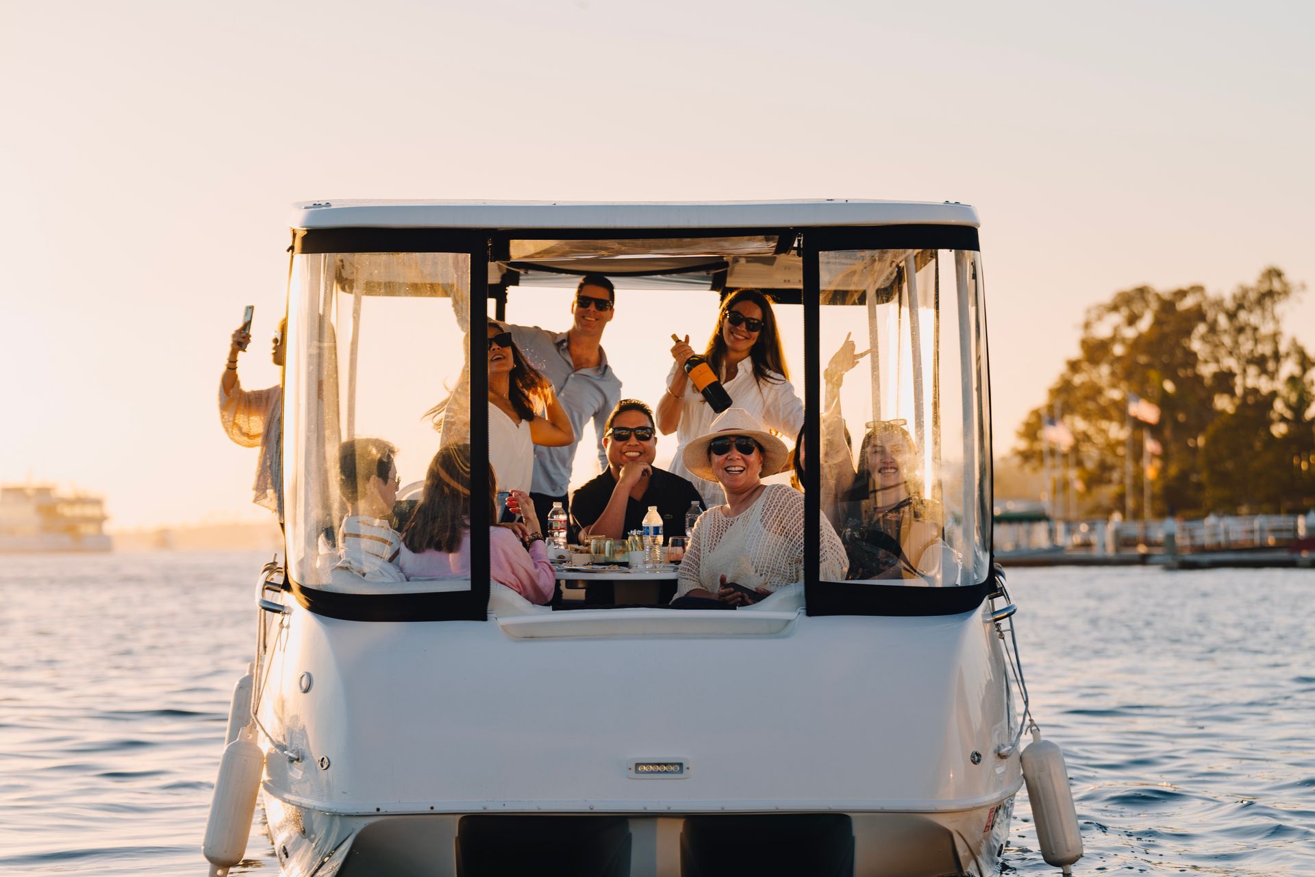 9 people in a white boat with a full transparent panel enclosure around them. someone in the background is taking a picture on their phone the rest of the people are smiling at the camera.