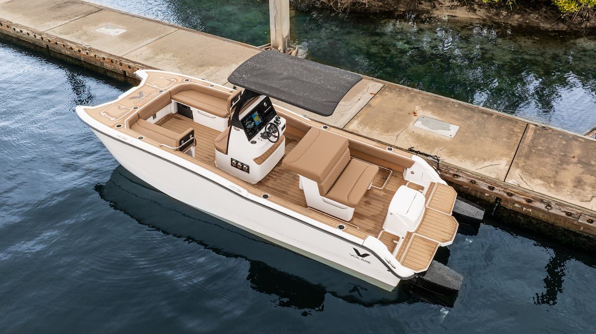 look down at A23 from Volare Boats. Black T Top and white hull with brown interior; it is docked by a boat ramp and has two motors on the back