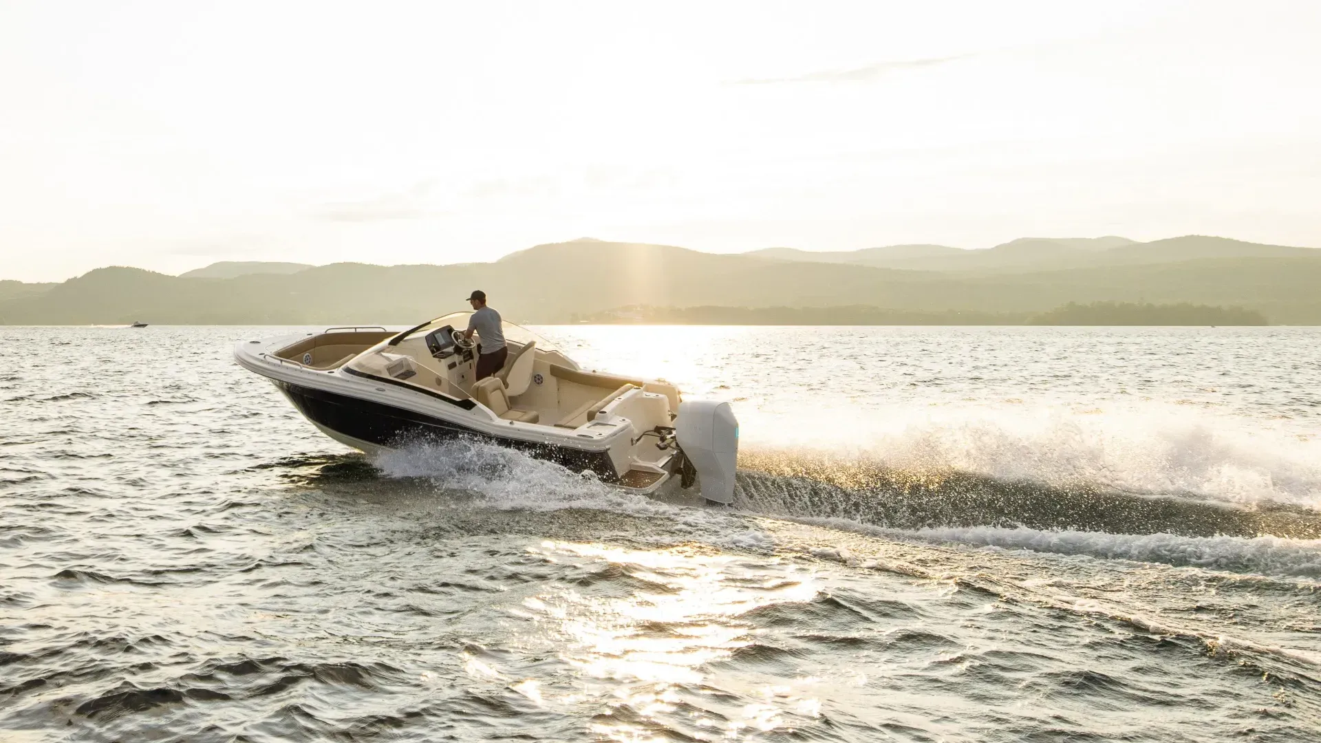 A man is driving a boat on a lake at sunset.