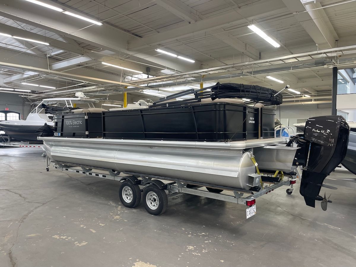black tritoon sitting in warehouse aluminum tubes and a black outboard motor that says FLUX in all capital letters in white