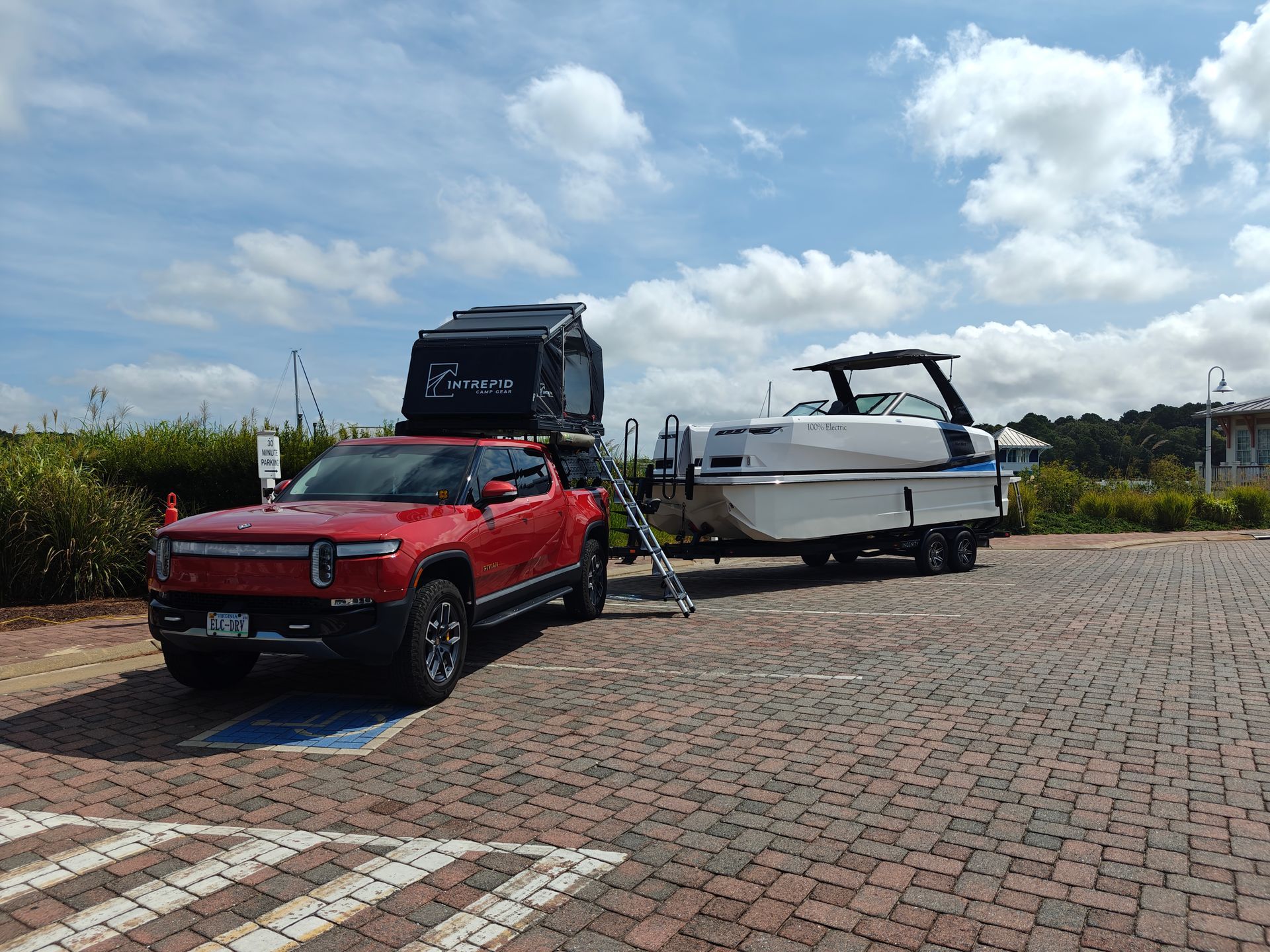 A red truck is towing a boat in a parking lot.