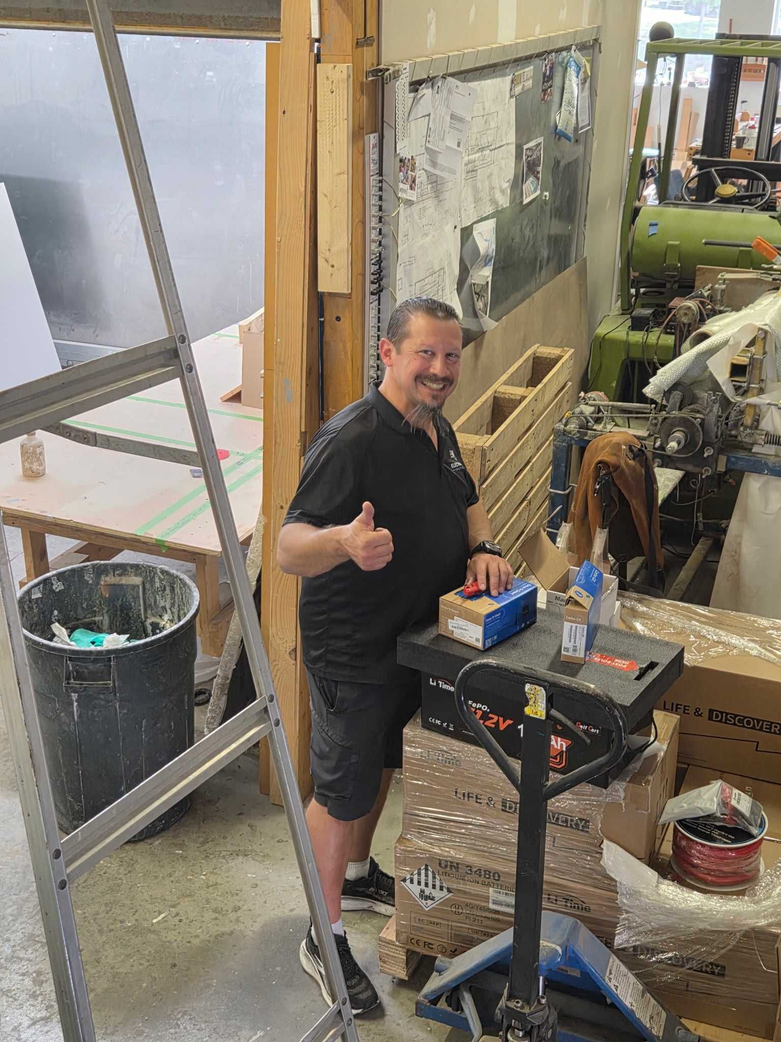 Man smiles at camera and gives a thumbs up in a warehouse with battery from LiTime visible.