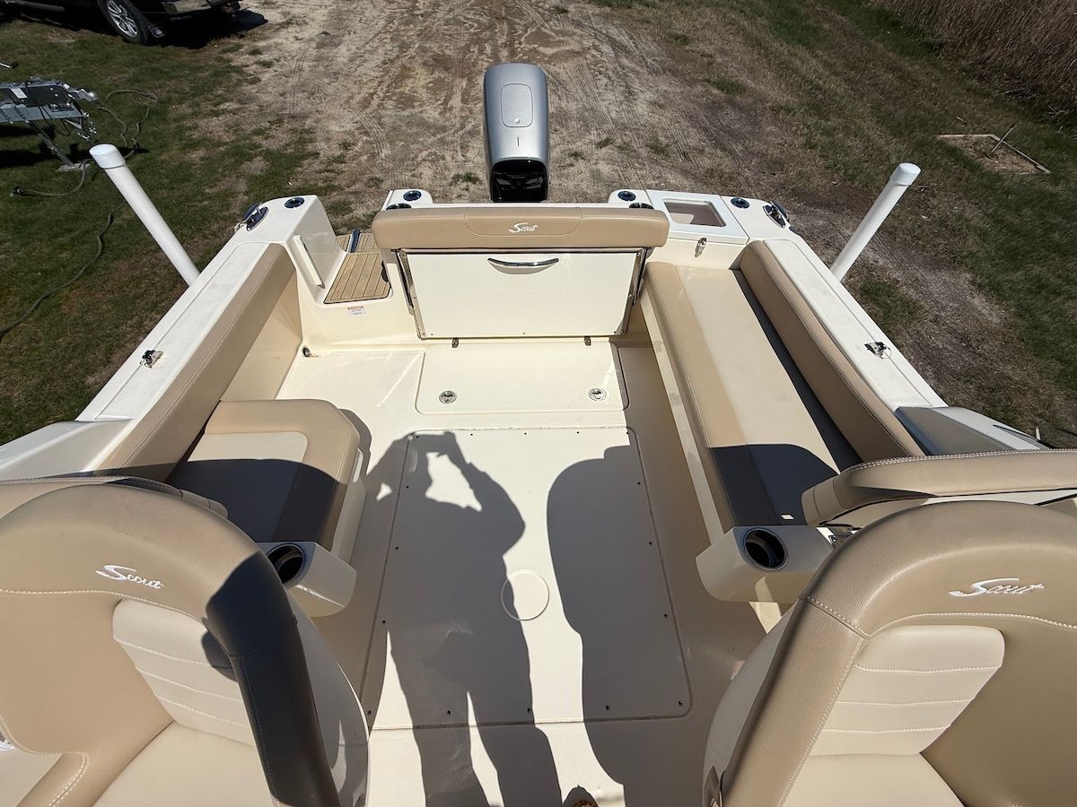 Inside the hull and layout of a Scout Dorado with light brown seats and cushions. The floor is white/cream and there is a shadow of a man taking a picture. There is a large grey outboard on the back of the boat.