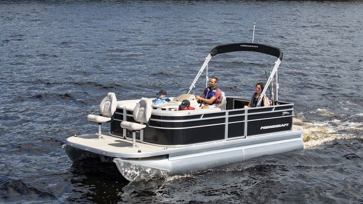 four people in a black pontoon two adults and two children. There are two seat at the front of the bow for fishing. the pontoon is slightly raised leaving a small wake.