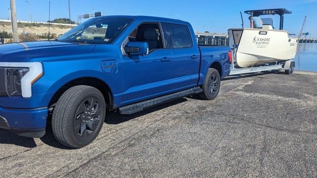 A blue truck is towing a boat on a trailer.