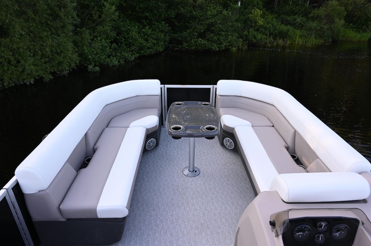 bow of a pontoon in the water, wrap around  cushioned seating with table set up and gate in the front