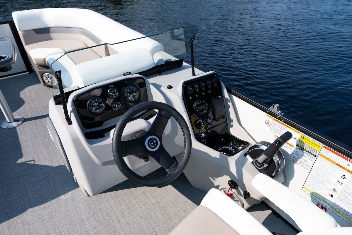 Helm of a pontoon with a steering wheel standard throttle and navigtion screen the helm is located on the starboard side 