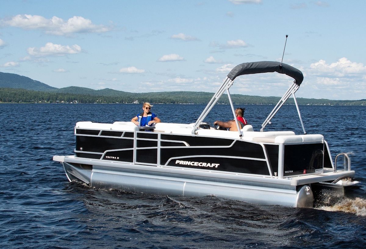 A man and woman are riding a pontoon boat on a lake.
