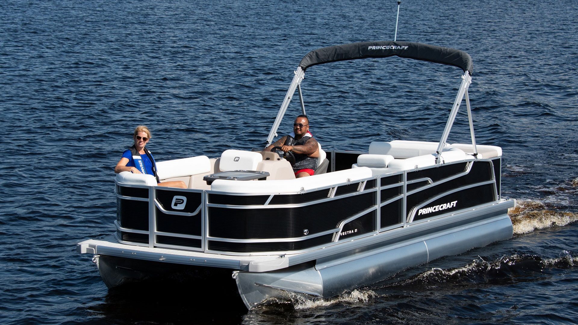 two people in a black pontoon the canopy is up but not extended they are in the middle of the water