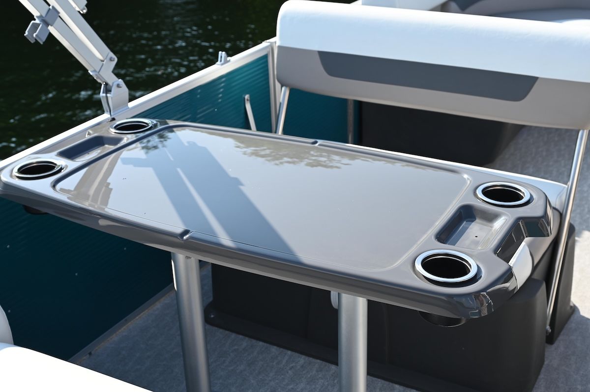Close up of grey plastic pop up table on boat with seating behind it. The table also has two stainless steel cupholders in the corner