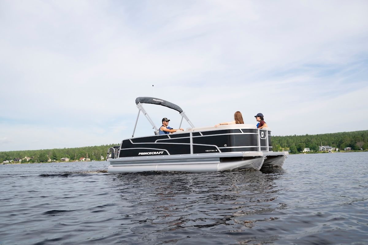 Three people aboard a black pontoon close to the shoreline, one captain and two passengers in the bow 