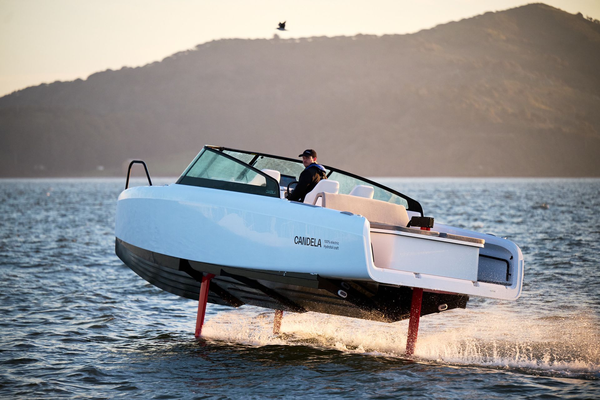 A man is riding a boat on a lake with mountains in the background.