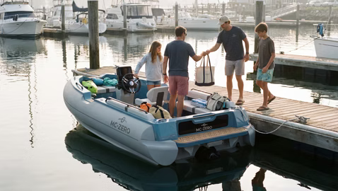 people on the dock getting onto a large tender with MCZERO on the side. Someone is handing a bag to a man on the boat.
