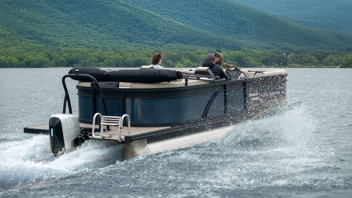 three people on board blue pontoon with Flux Marine outboard motor on the back with blue indicator light on. There are mountains in the background covered in green foliage.