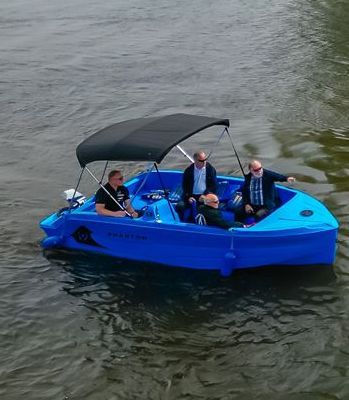 Three men in a smaller blue boat with a black canopy up covering the people in the boat.