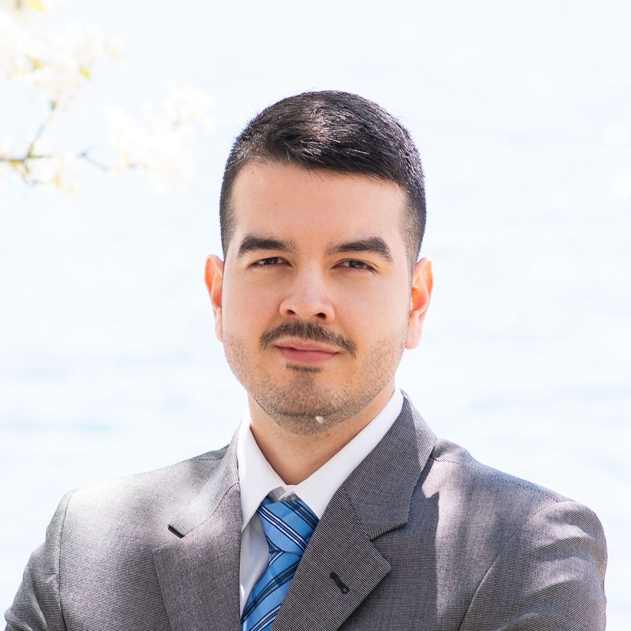 Portrait of a man in a gray suit and blue tie outdoors in bright sunlight