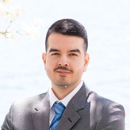 Portrait of a man in a gray suit and blue tie against a bright outdoor background