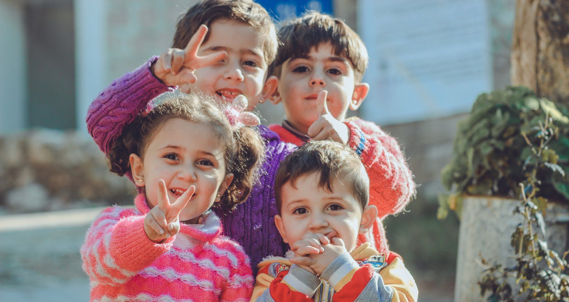 Four children smiling and holding up colorful snacks outdoors in bright sunlight