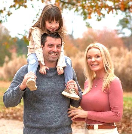 A man and woman are holding a baby on their shoulders in a park.