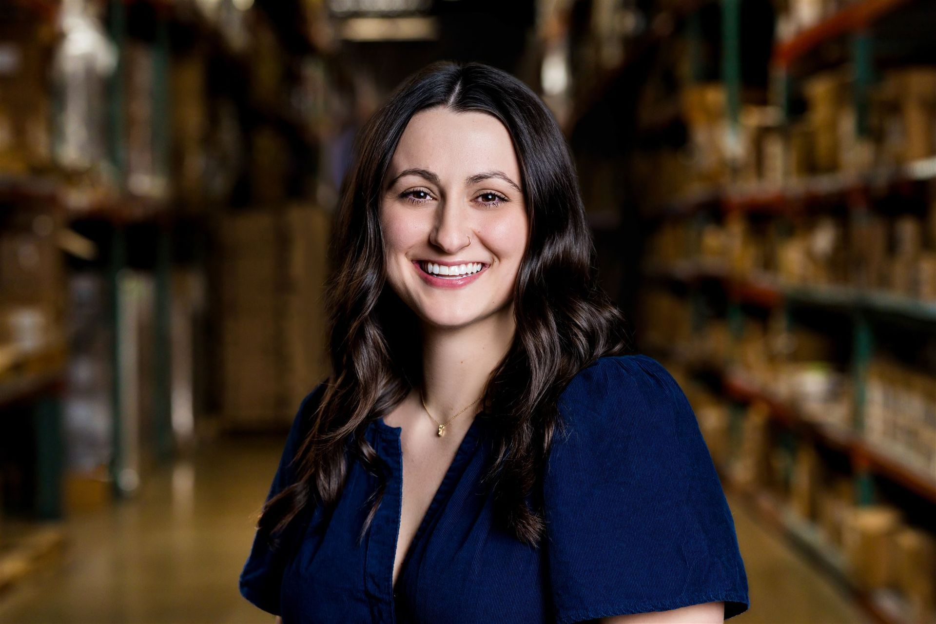 Smiling woman in a blue shirt standing in a bookstore aisle with shelves blurred behind her
