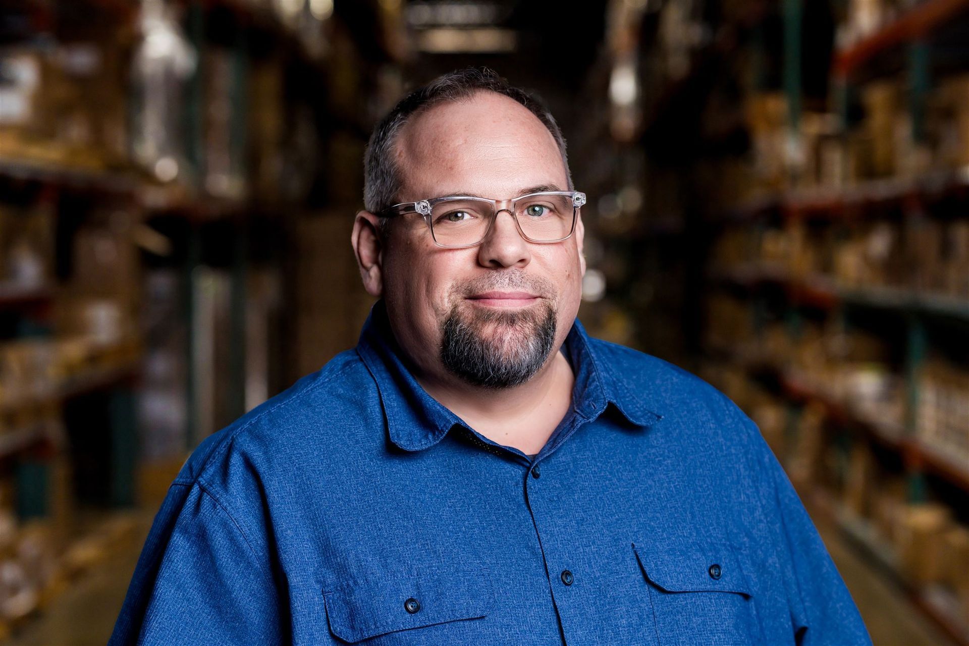 Man in a blue shirt standing in a store aisle with shelves blurred in the background