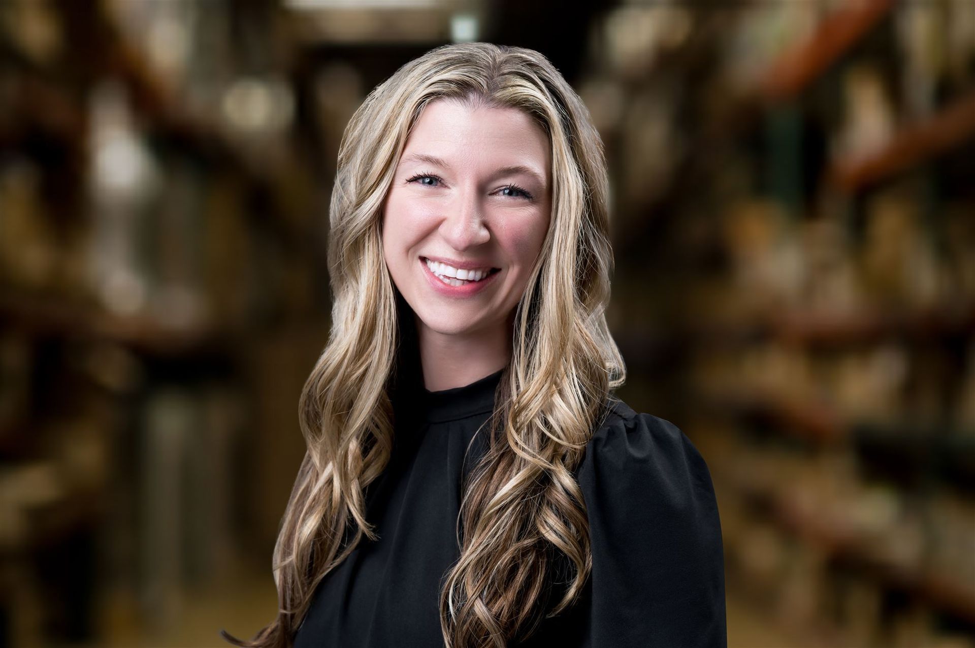 Smiling woman in a black top standing in a warehouse aisle with shelves in the background