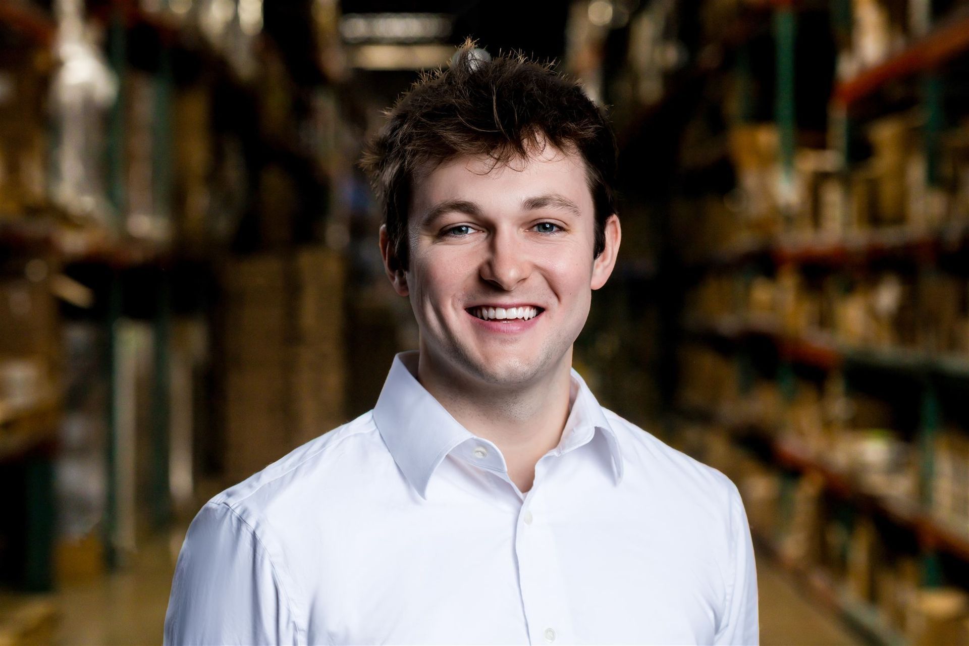 Smiling man in a white shirt standing in a blurred warehouse aisle