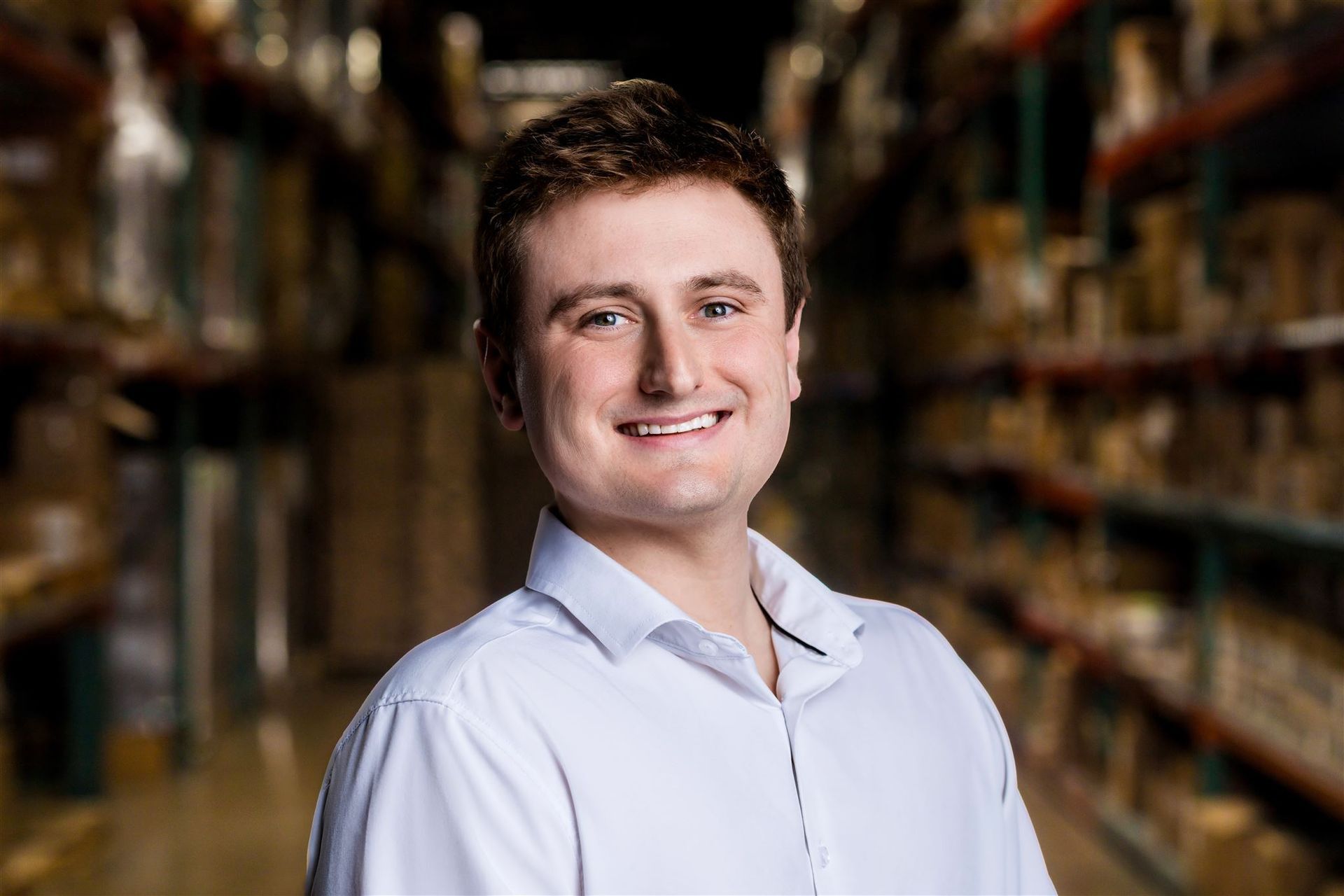 Smiling man in a light blue shirt standing in a warehouse aisle with shelves in the background