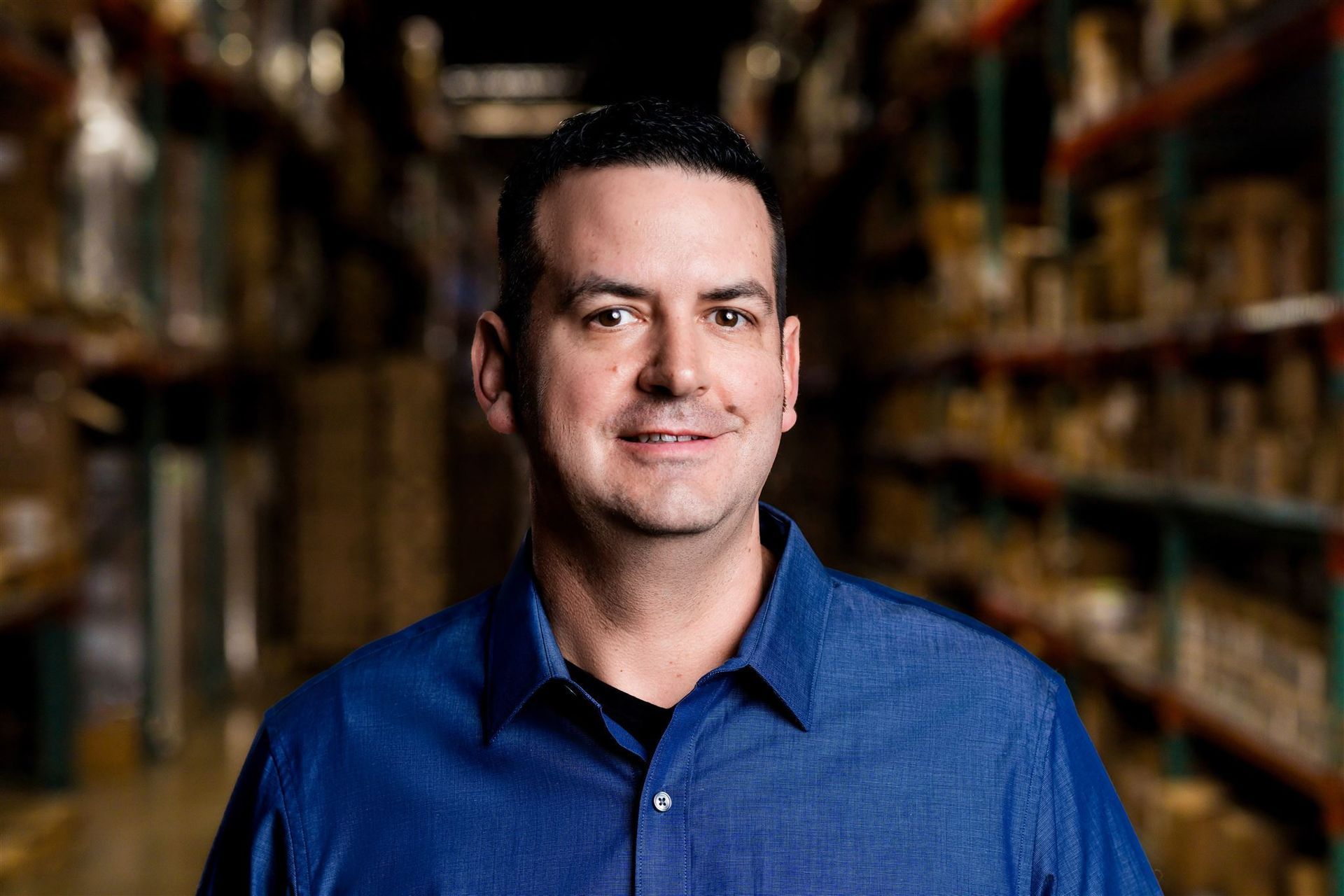Man in a blue shirt standing in a store aisle with shelves blurred in the background