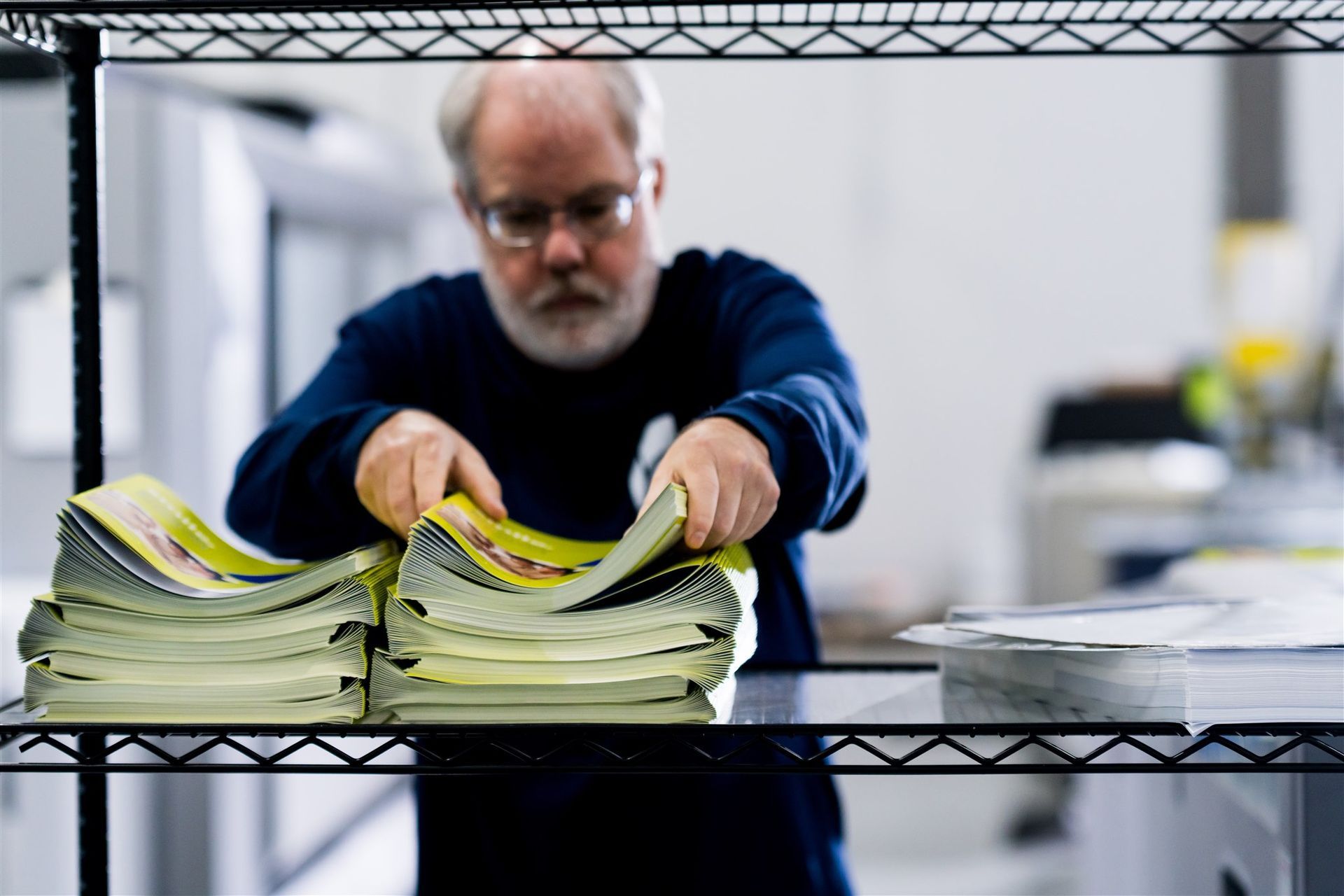 Man sorting stacks of yellow papers on a metal shelf in an office setting