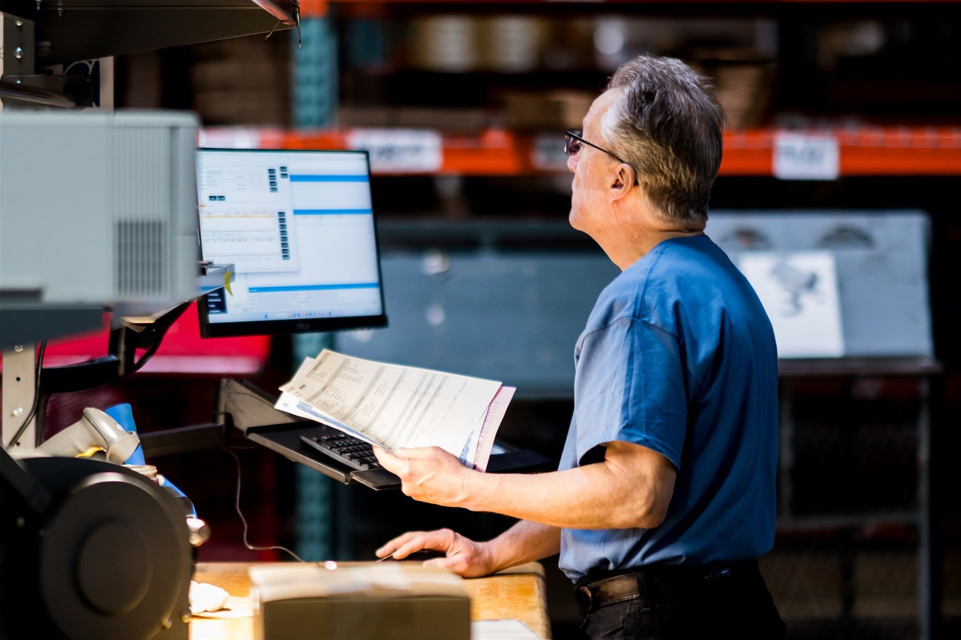 Person at a warehouse desk using a computer and reading papers