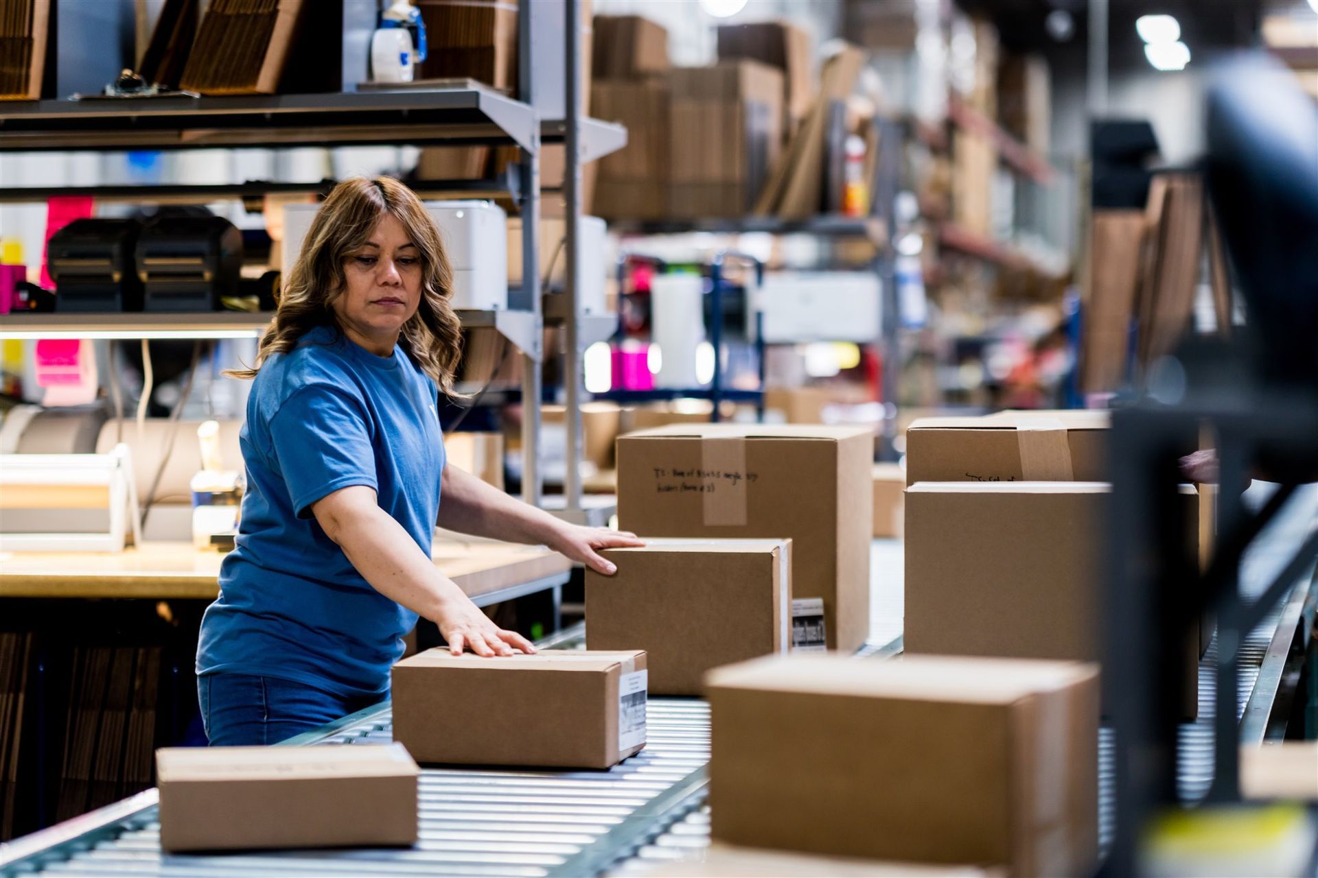 Worker in a blue shirt sorting boxes on a warehouse conveyor belt.