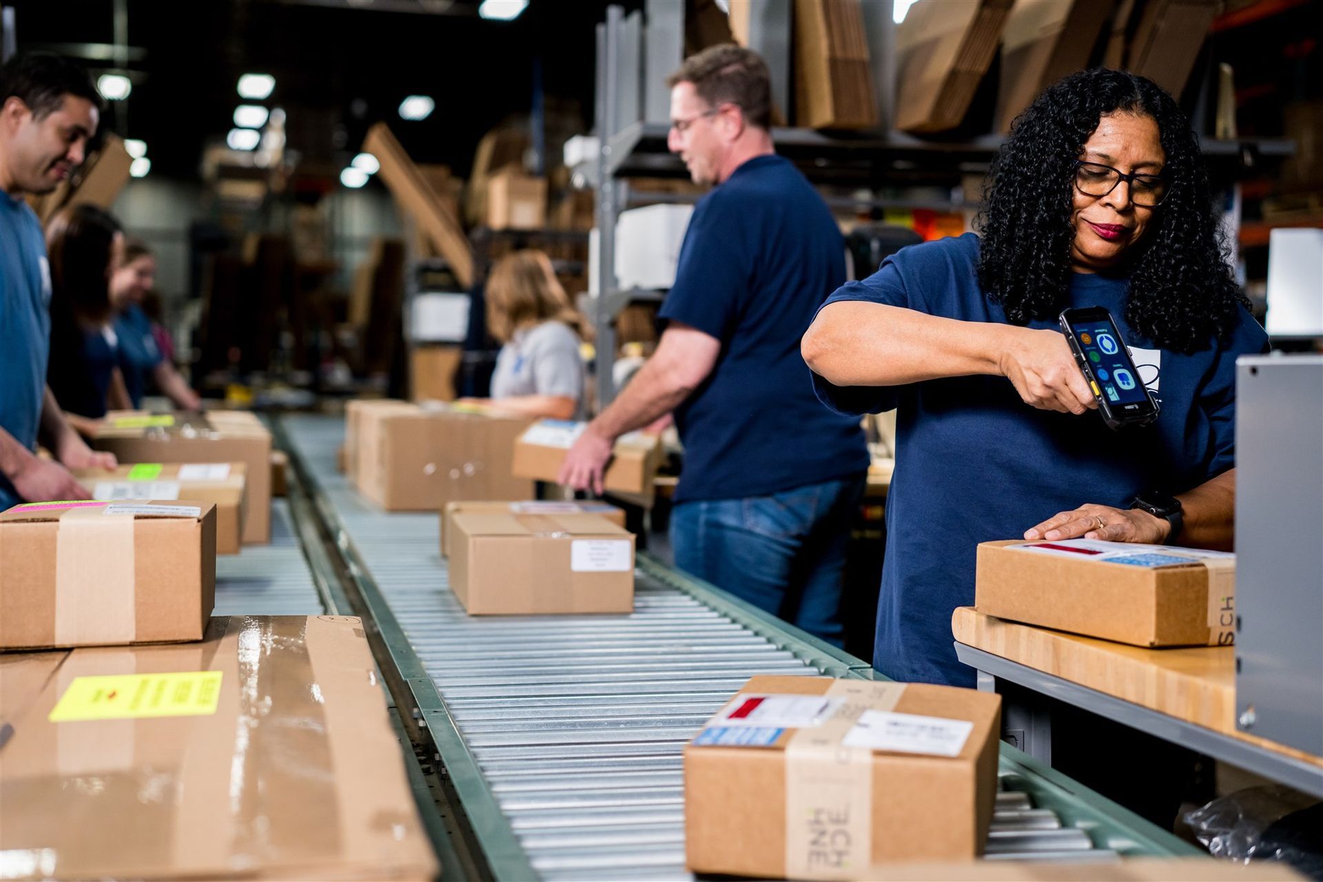 Workers packing cardboard boxes on a conveyor belt in a warehouse shipping area