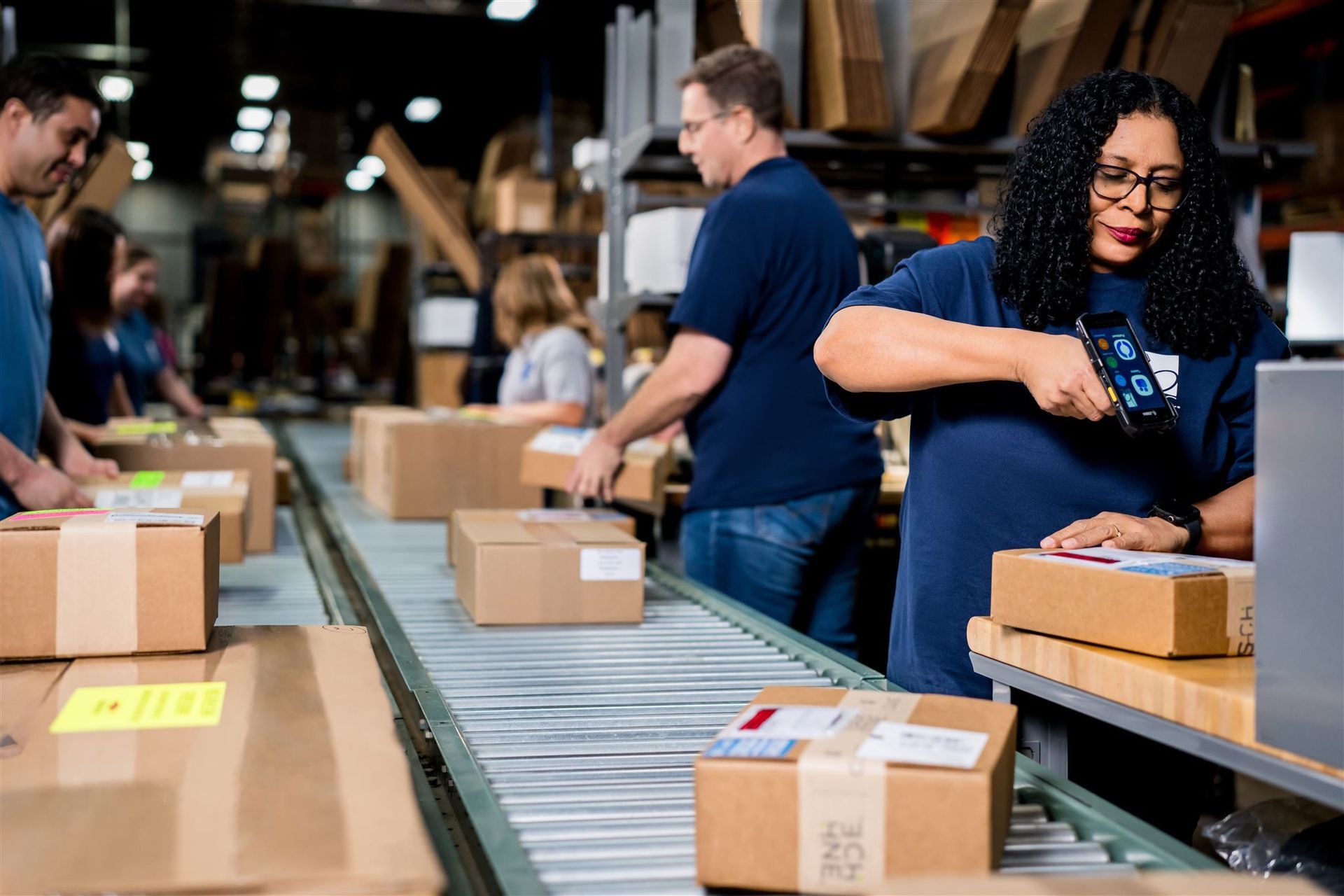 Workers packing cardboard boxes on a conveyor belt in a warehouse or fulfillment center